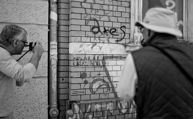 "Fuck capitalism" sign being photographed in East Berlin. Leica M9 with Leica 35mm Summilux-M AA f/1.4. © 2016 Thorsten Overgaard.  