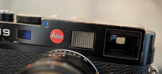 The Rangefinder

The rangefinder on the Leica M is the cooperation between the viewfinder (to the right) and the small rangefinder eye (to the left of the logo) in the picture above.

The rangefinder works very closely, and with exceptional mechanical precision, with the large viewfinder window to the right in the picture above. 

When the focusing ring on the lens is turned, the chrome metal wheel inside the camera is pressed, and that chrome metal wheel moves a prism that mirrors what the small rangefinder eye sees. 

It is the reflection of that small rangefinder eye that you see in the middle of the large rangefinder window. When it lays on top and matches the rest of the image, the image is in focus.

It's 100% mechanical and one of the few wonders of this world that still impress people. 

Here is a drawing - seen from the inside/back of the camera that shows how the mechanism works: