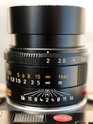 Aperture ring

The front ring on a Leica lens is the aperture adjustment. Each number is a "stop" and most lenses have a click in between the numbers that is a "half stop". 

Focus ring

The focus ring has meters in white and feet in orange (sometimes red).

Depth of Field

The lines and numbers closest to the body shows the depth of field at different aperture stops. Note that for the infinity symbol (the 8 lying down), the actual infinity distance is in the middle of the 8. So if you wanted to set the lens to f/16 and make sure you got the most in focus, you would put the center of the 8 above the line of 16. 