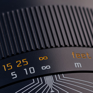 Infinity-symbol (∞)  and distance scales  The manual focus scale goes from 2.8 feet / 85 cm to "infinity", which is marked with the ∞ symbol.   The focusing barrel has two scales. An orange for feet and a white for meters. Before 1950, some Leica lenses had only one scale, so there were models for some countries shown in meters and other models for other countries shown in feet. At some point some genius figured both scales could be on the lens. 