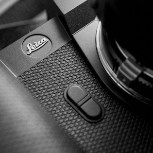 Two Function buttons on the front of the Leica SL2

The two buttons on the front are Fn buttons (Function button) which you can program to your likings. 

By default, from factory, the top one zooms into the imagre (press it; and if you turn the thumbs wheel you can change the zoom ration).

The bottom one is default from factory a selection for AF mode - you can change it from spot to multi-field and so on. 

