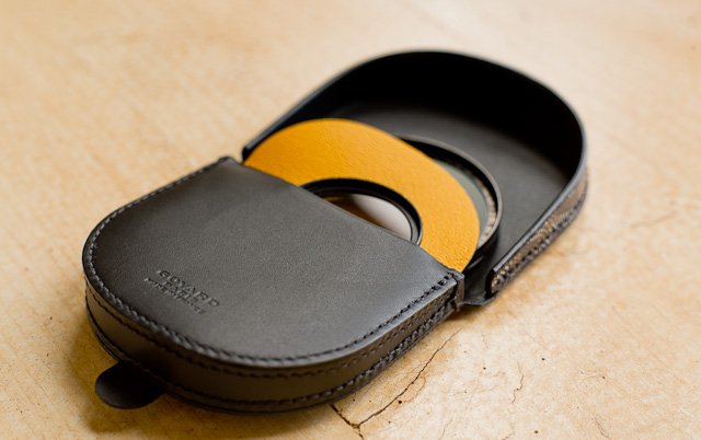 The Goyard coin wallet in leather and canvas holds two filters. In this photo a 60mm and a 39mm filter occupy the two compartments. One of the compartments is yellow inside. 