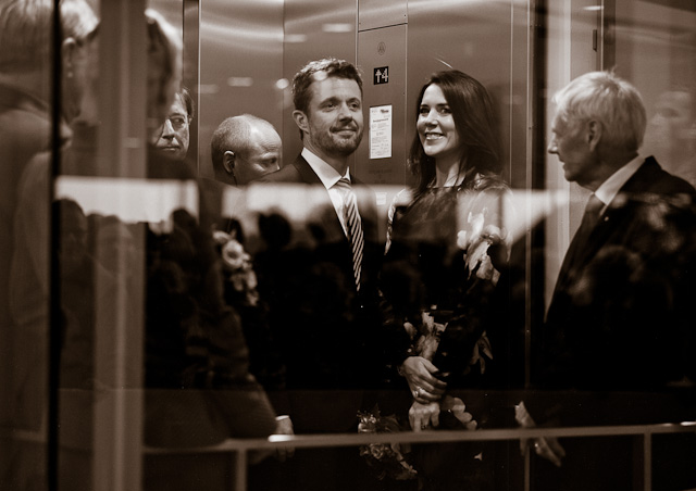 Behave as if you aren't Royal: The Crown Prince Couple Frederik and Mary, and Queen Margrethe in a glass elevator, waiting like any other family for the elevator to depart ... with a crowd watching outside. Leica M240 with Leica 90mm APO-Summicron-M ASPH f/2.0. © Thorsten von Overgaard.