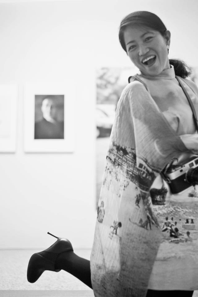 Malou Lasquite wearing a dress straight from Prada’s 2010 spring/summer runway collectionwith a large black and white beach photograph for the vernissage. Photo by Pierre Pallez. Around her neck, a silver Leica M9-P.